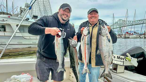2 smiling men standing on Legion's Mercy, Lance Fisher's 34' guide boat, holding up their Chinook and Coho salmon.